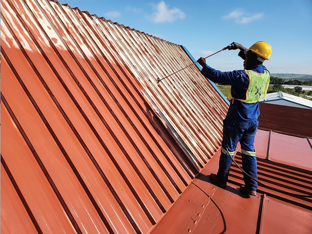 Professional worker spray painting factory roof with red waterproof coating